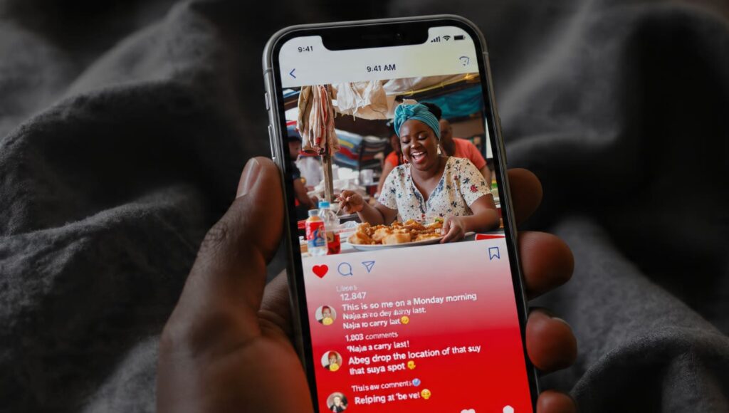 A hand holding a smartphone showing an Instagram post with over 1,000 comments and vibrant community discussion about a local food spot.