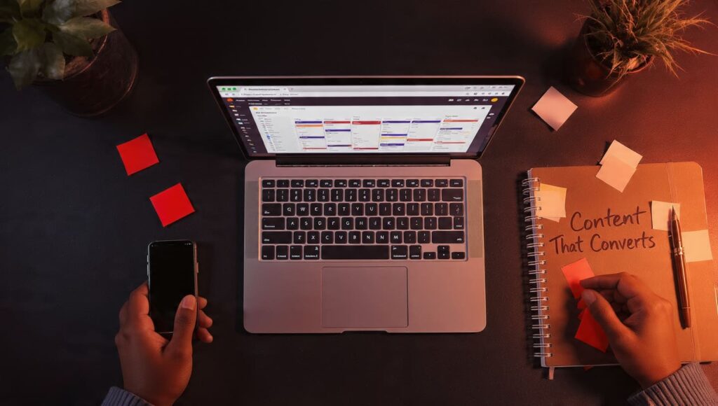 Overhead view of a workspace featuring a laptop with a content calendar, a smartphone, and a "Content That Converts" notebook