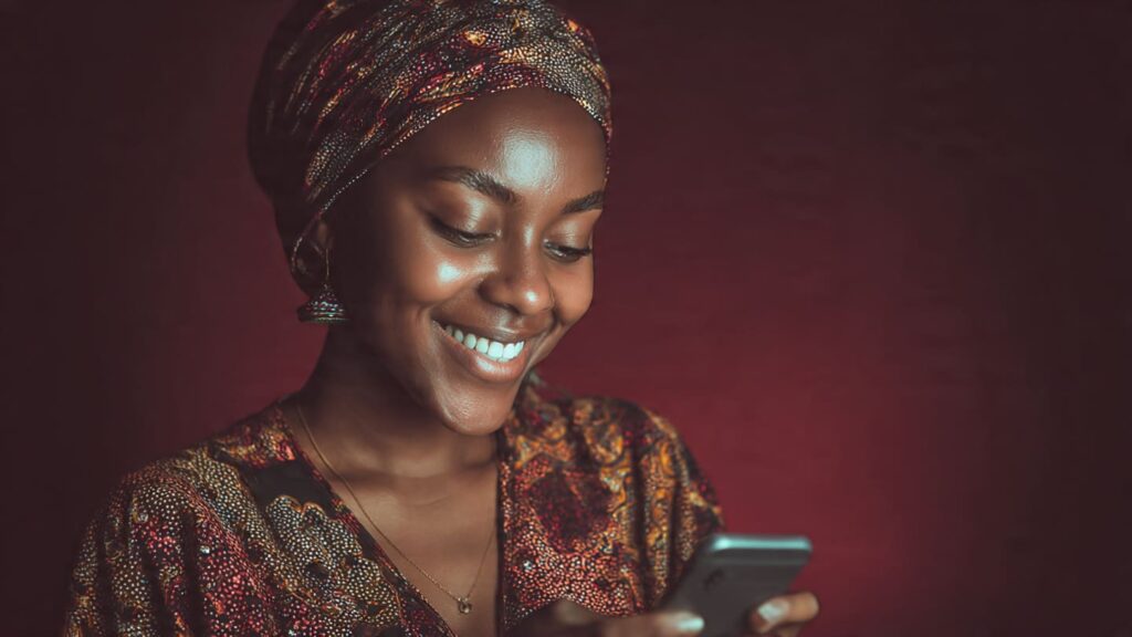 A close-up of a Nigerian woman smiling and Instagram comment growth strategies in Nigeria while reading a flurry of positive comments on her smartphone.