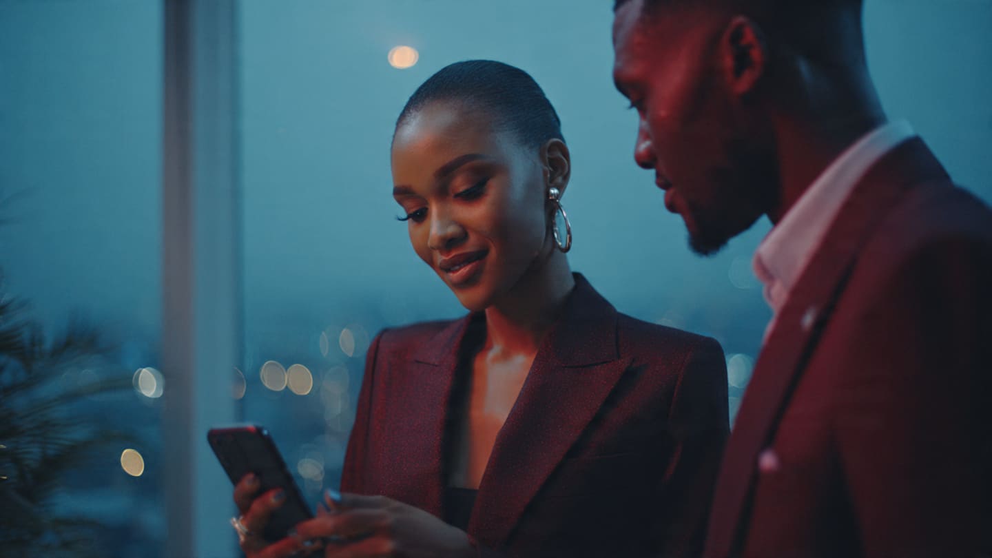 A successful Nigerian female entrepreneur in a red blazer looking at her viral Instagram Reels engagement metrics on a smartphone.