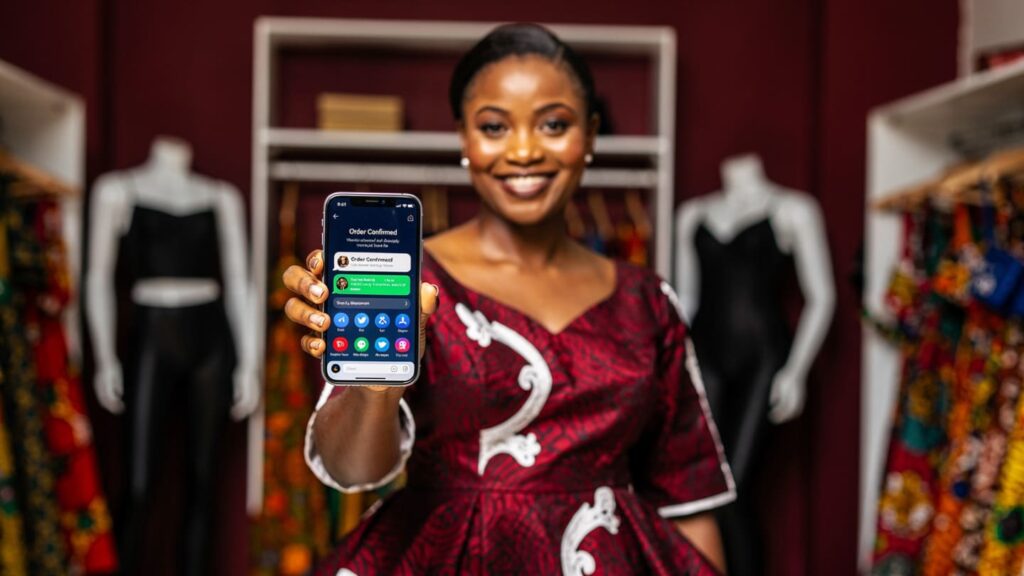 A happy Nigerian boutique owner holding a phone showing high sales and engagement notifications.
